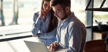 Two colleagues looking at a computer and discussing business.