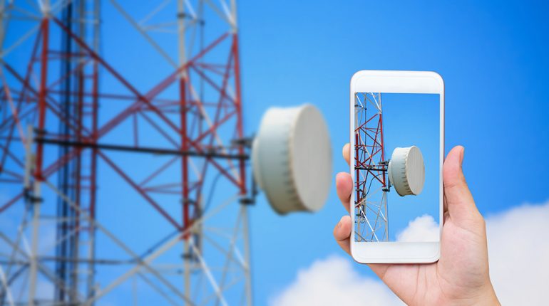 hand hold mobile smartphone with telecommunication tower hand hold mobile smartphone with telecommunication tower and satellite antennas wireless technology on blue sky background