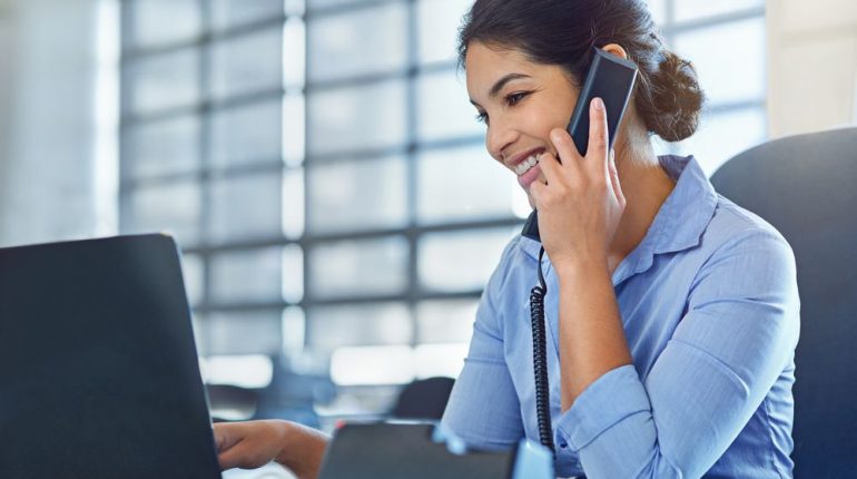 Shot of a young businesswoman talking on the phone while using a laptop at work